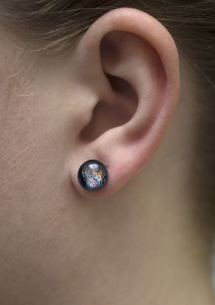 Small dichroic glass stud earrings on a model
